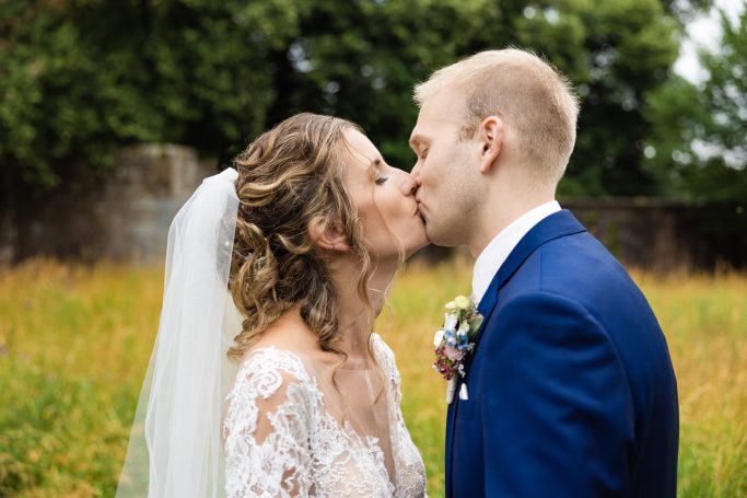 Hochzeit Heilbronn – Brautpaarkuss in blühender Wiese Ein Brautpaar küsst sich in einer blühenden Wiese, umgeben von Natur.