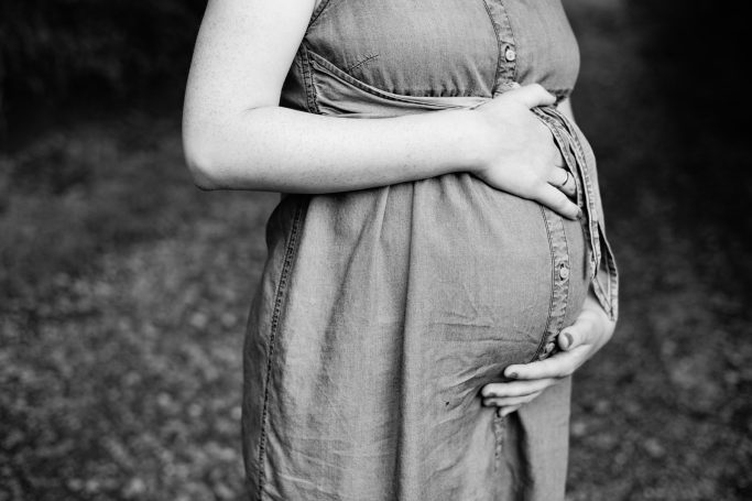 Eine schwangere Person in einem eleganten Kleid hält sanft ihren Bauch.