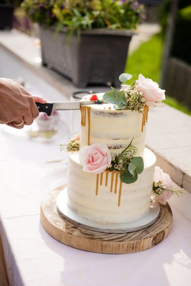 Zwei-stöckige Torte mit Karamellüberzug und Blumen, wird angeschnitten.