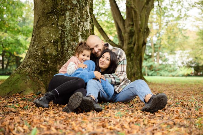 Drei Personen sitzen um einen Baum, umgeben von Herbstlaub und Natur.