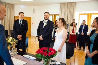Hochzeitszeremonie mit Braut, Bräutigam und Gästen in einem hellen Raum.