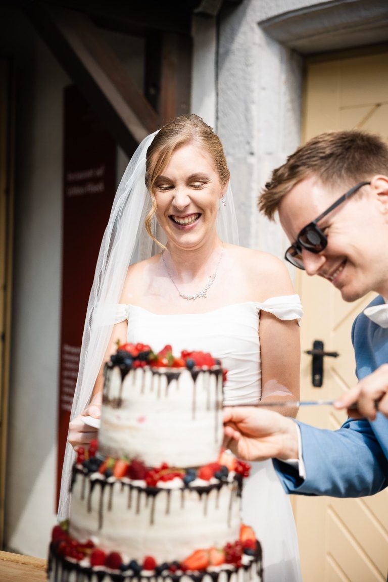 Die Braut lacht weil der Bräutigam die Torte schneidet