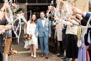 Frisch verheiratetes Brautpaar läuft aus dem Standesamt Heilbronn – Gäste stehen Spalier, werfen Blumen oder Reis, fröhlicher Hochzeitsmomen