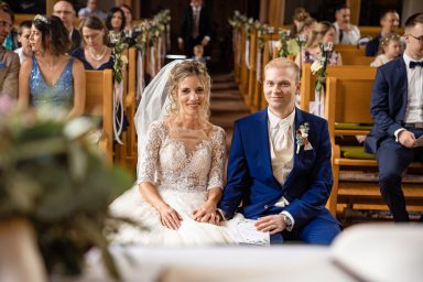 Brautpaar sitzt bei der Trauung in der Kirche und schaut in die Kamera des Fotografen.